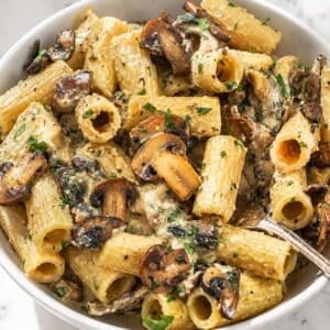 Hummus pasta with a fork and browned mushrooms, parsley, Parmesan, and black pepper.