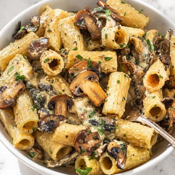 Hummus pasta with a fork and browned mushrooms, parsley, Parmesan, and black pepper.