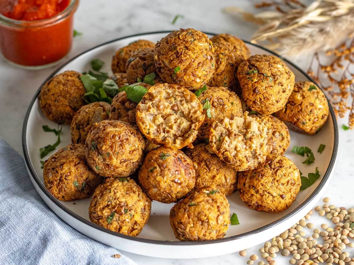 Lentil meatballs served as an appetizer on a white plate with marinara sauce.