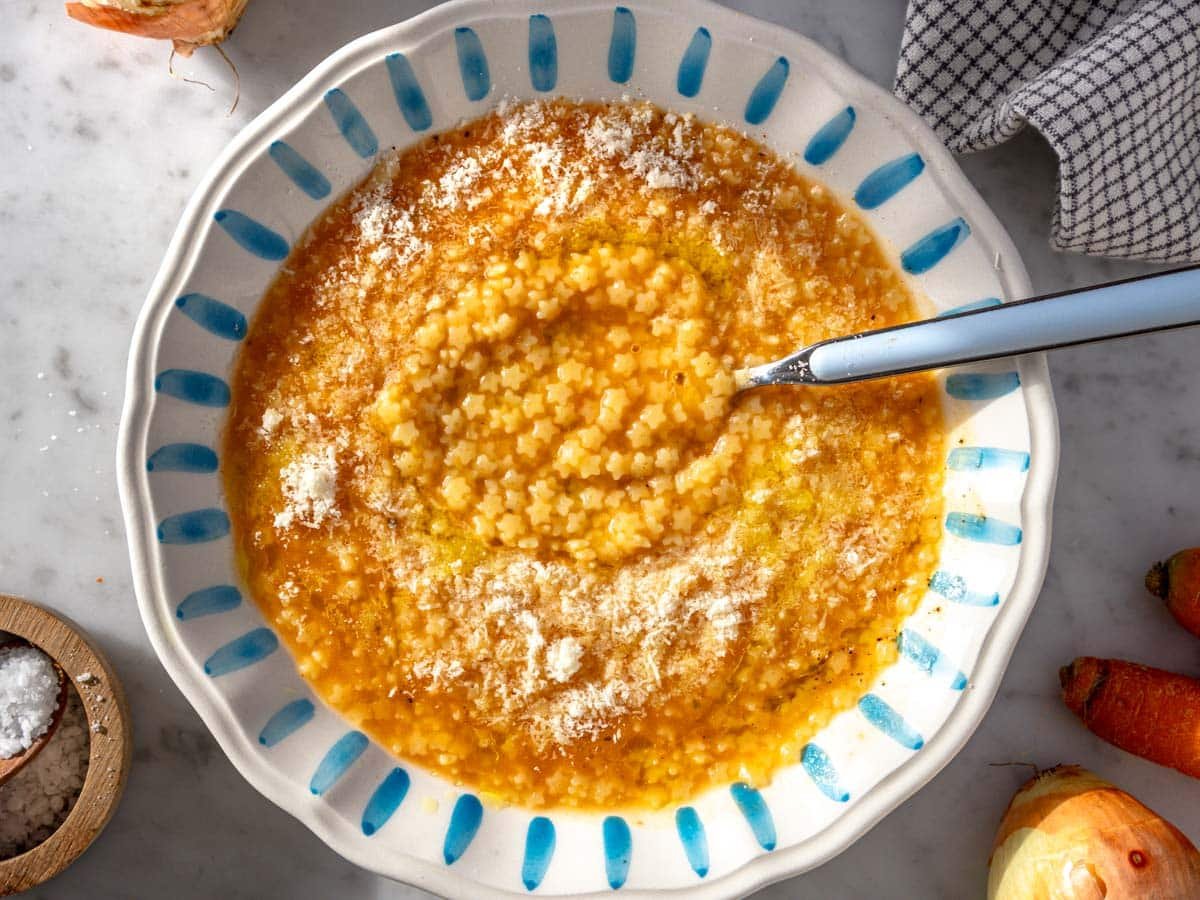 Pastina soup with parmesan cheese with a blue spoon.