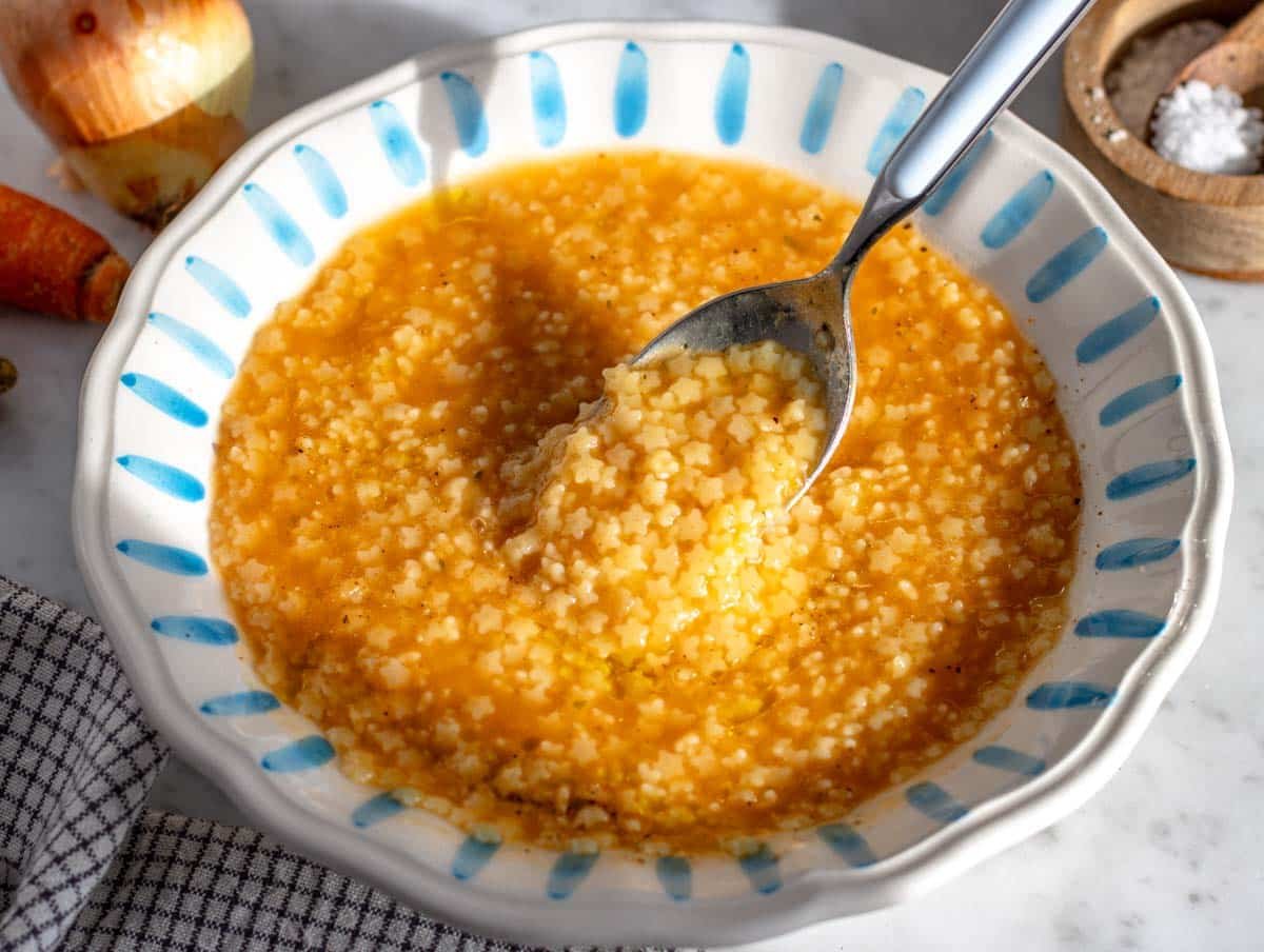 Pastina with a blue spoon in a white and blue bowl.