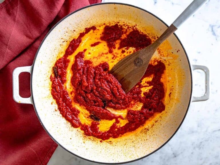 Tomato sauce cooking in a white skillet with a wooden spatula.