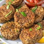 Golden lentil patties with visible lentils stacked with fresh parsley and lemon on a white plate.