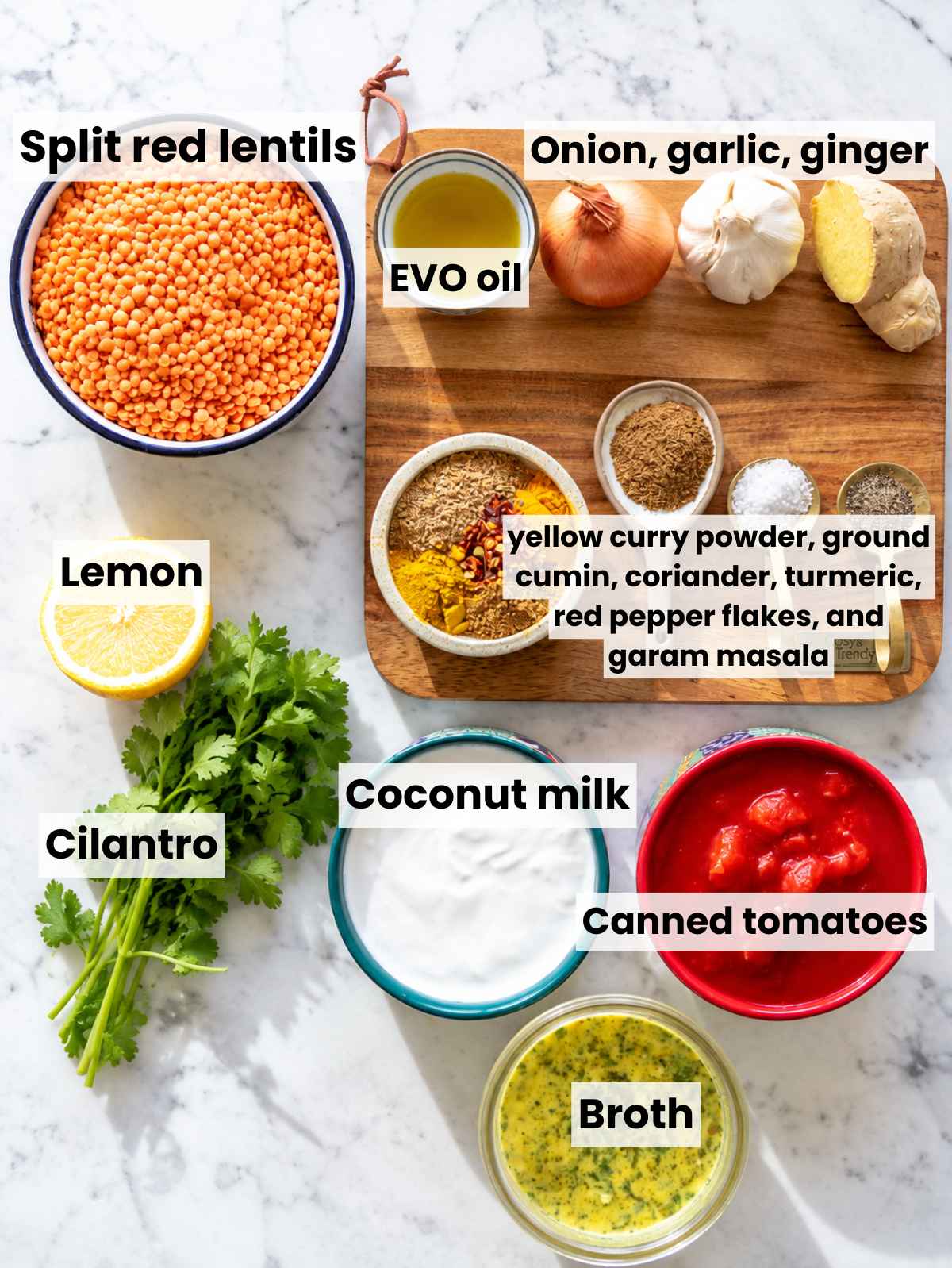 Lentil curry ingredients with red lentils, coconut milk, tomatoes, aromatics, and spices on marble