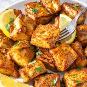 Plate of golden marinated tofu on white marble in natural daylight.