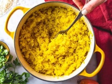 Female hand with a fork in saffron rice.
