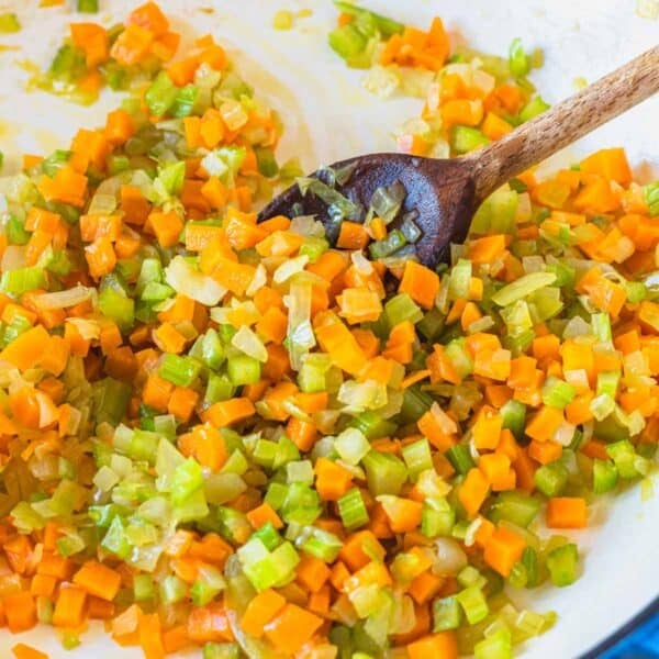 Soffritto in a white skillet with a wooden spoon.