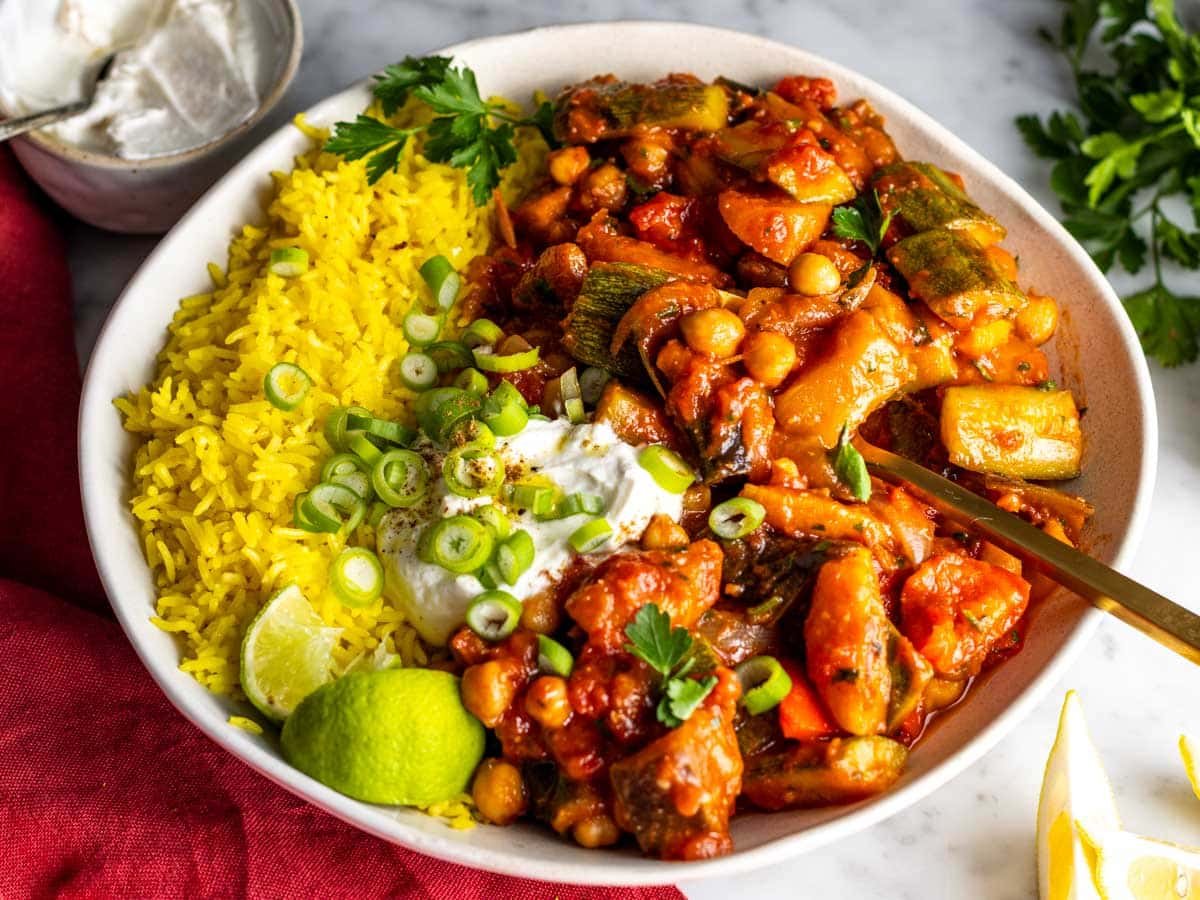Tagine in a white bowl served with saffron rice, yogurt, and fresh herbs.