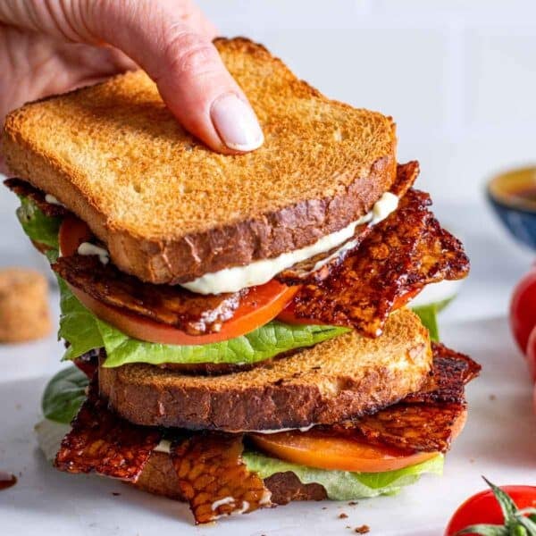 Tempeh bacon in a BLT sandwich and a hand.