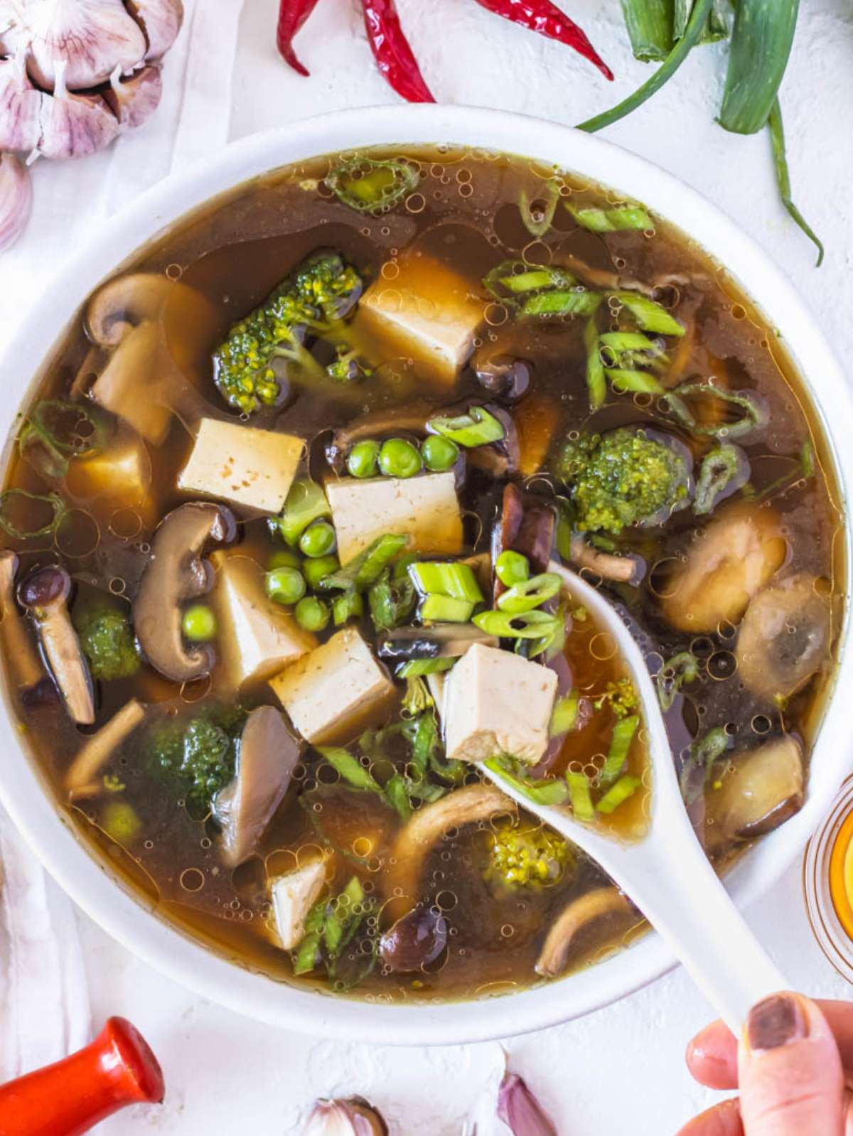 Top down view of tofu soup with noodles and broccoli in white bowl.