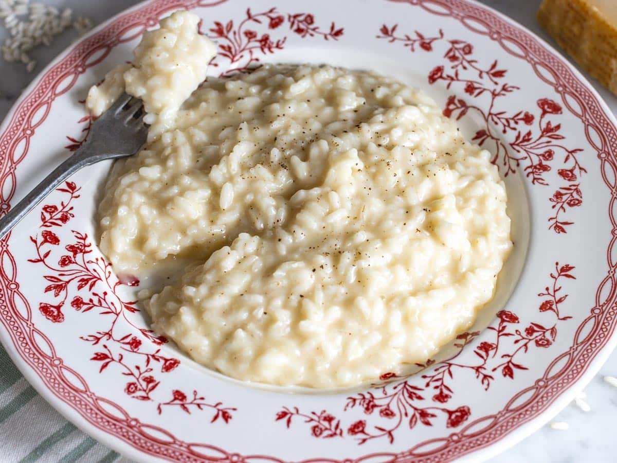 Parmesan risotto served on a red plate with a silver fork.