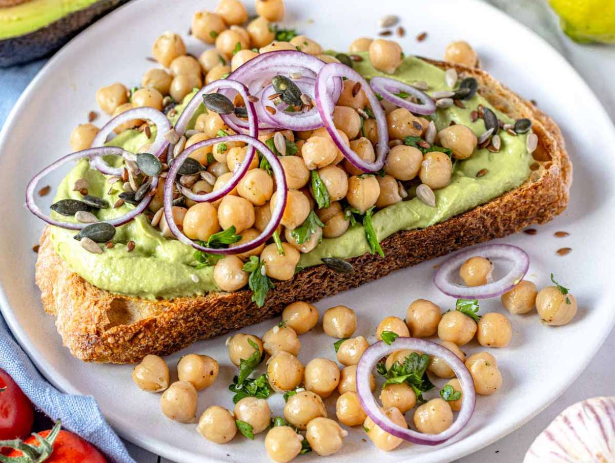 Avocado spread on a slice of toasted bread topped with marinated chickpeas.