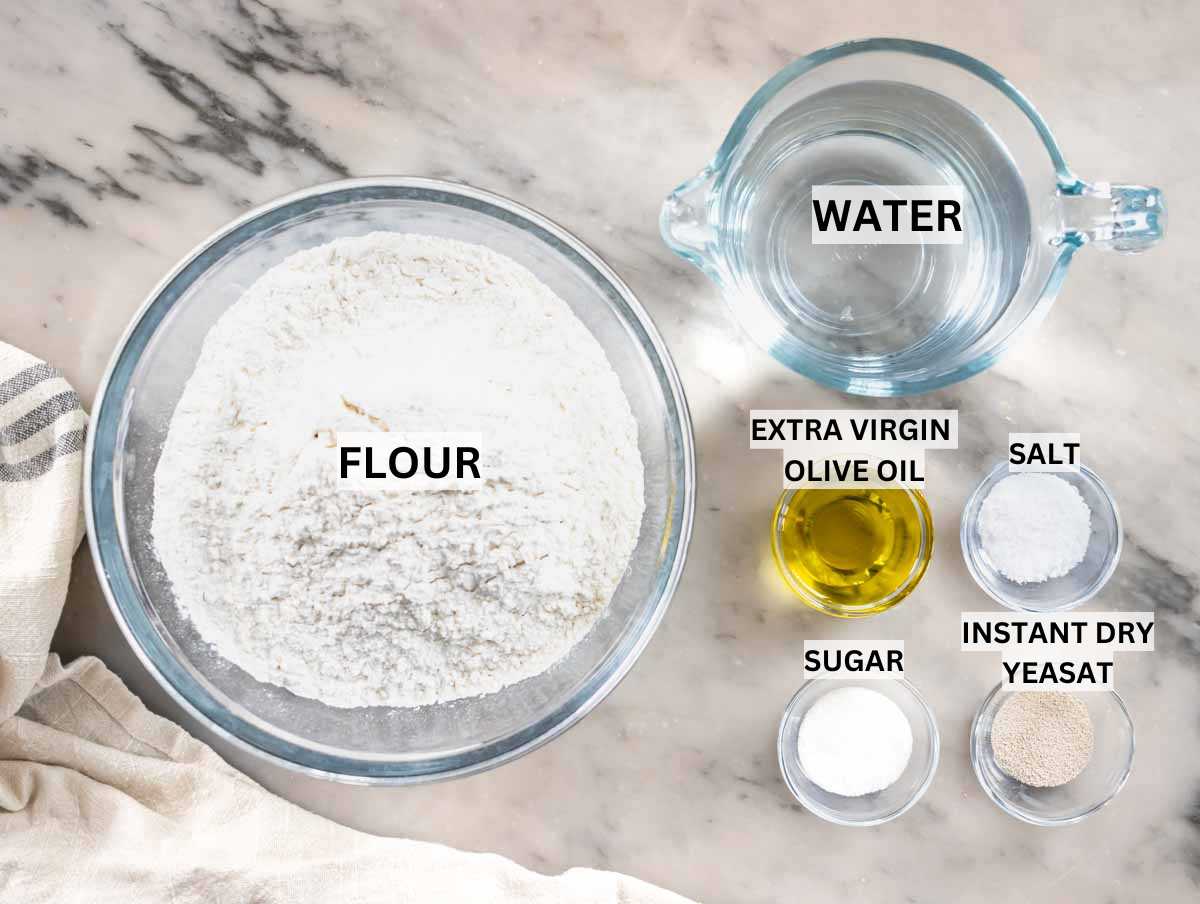 Ingredients for homemade focaccia on a marble table.