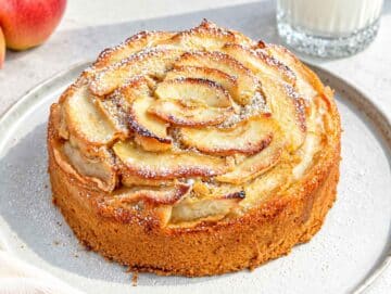 Step 4 Golden vegan apple cake cooling on a plate with baked apple topping.