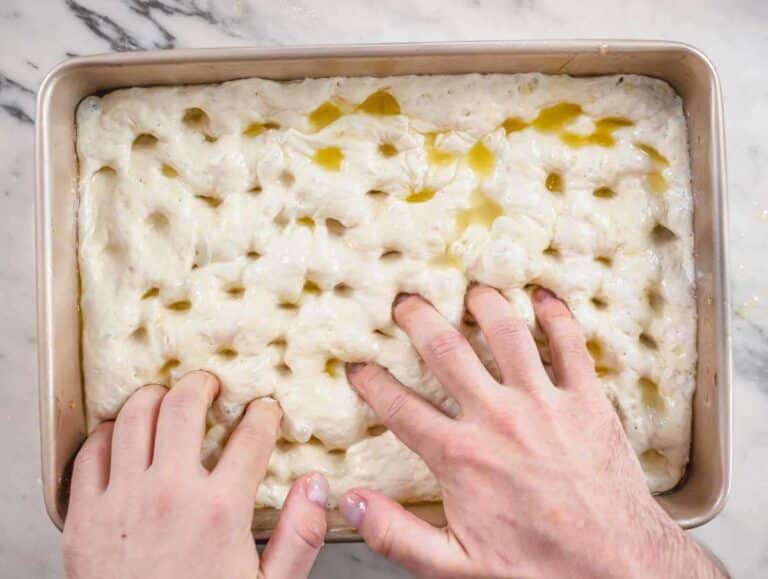 Step 6 Fingers pressing deep dimples into focaccia dough with oil mixture.