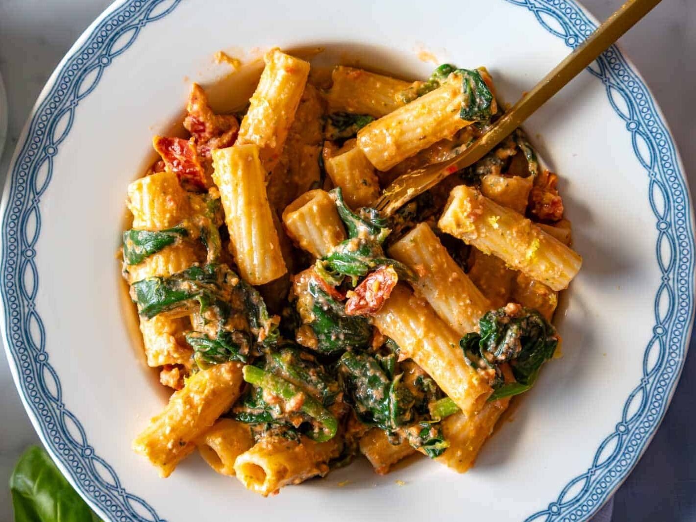 Sun dried tomato pasta with spinach on a blue plate.