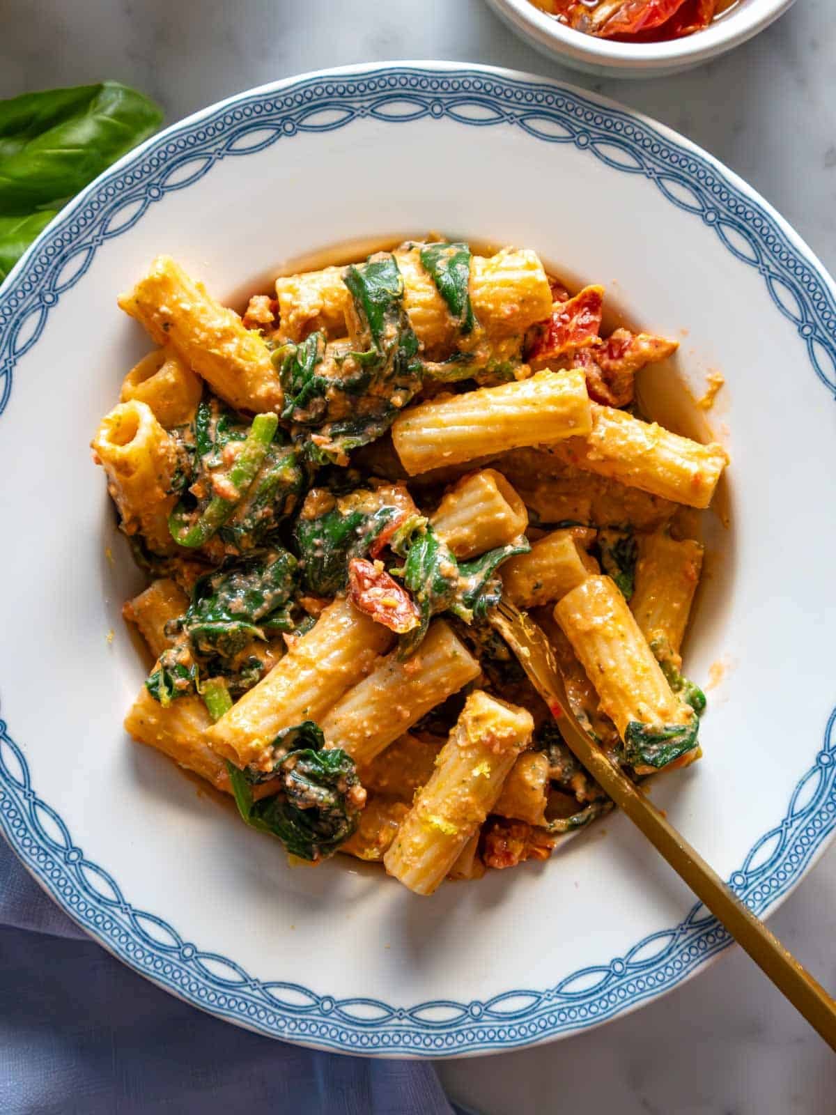 Sun dried tomato pasta with spinach on a blue plate.