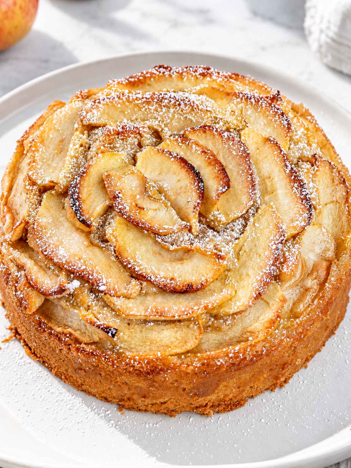Whole vegan apple cake topped with overlapping cinnamon apple slices.