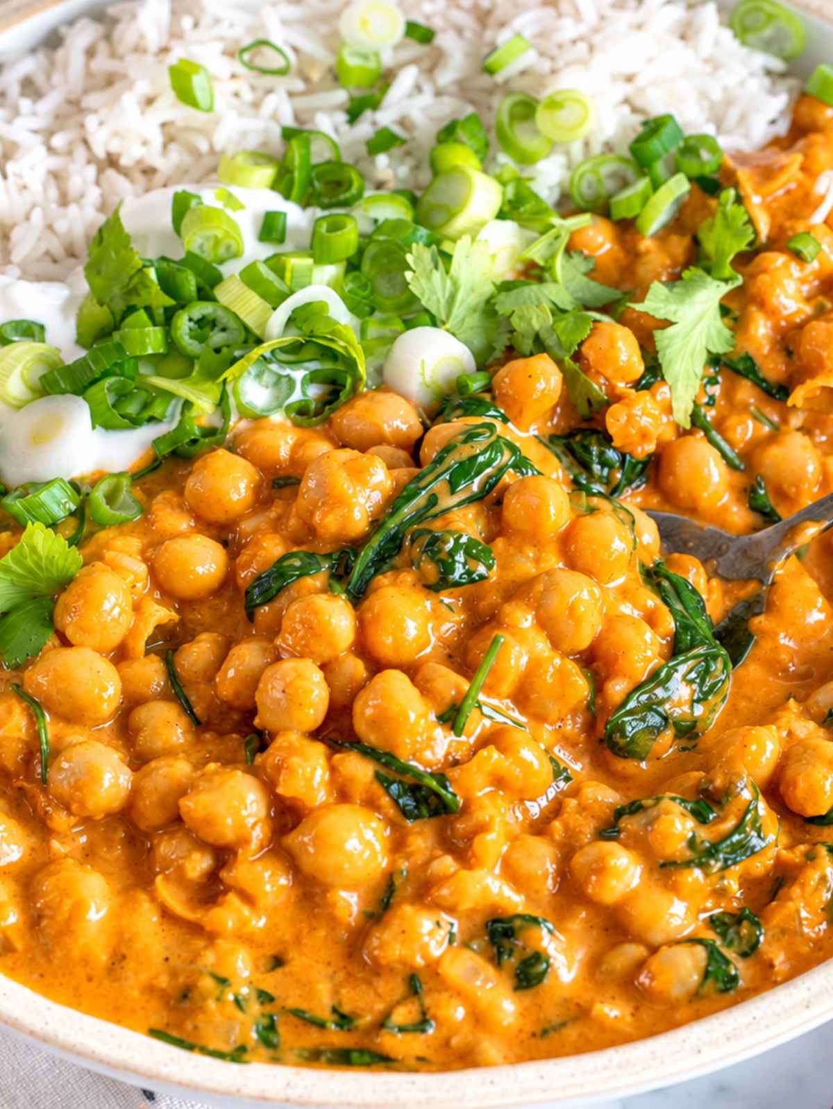 Close-up of tender chickpeas and wilted spinach coated in golden curry sauce.