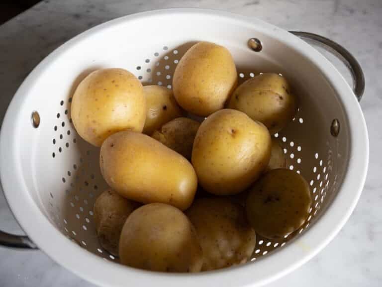 Boiled potatoes steaming off in a colander.