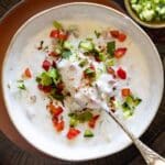 Raita in a bowl garnished with ground cumin and cilantro.
