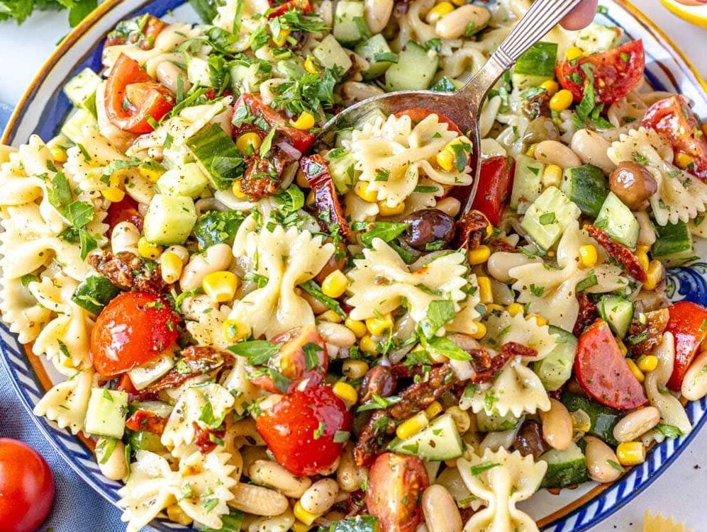 Vegan Pasta Salad on a blue plate with hand holding a silver spoon
