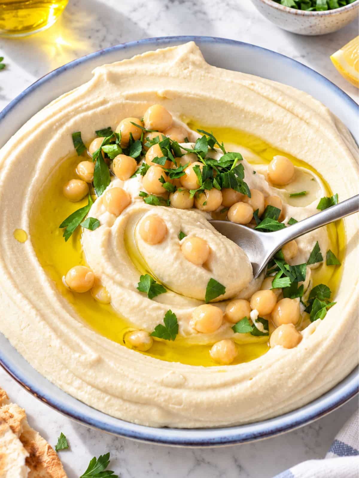 Close up of smooth hummus showing its silky texture, olive oil, chickpeas, and parsley.