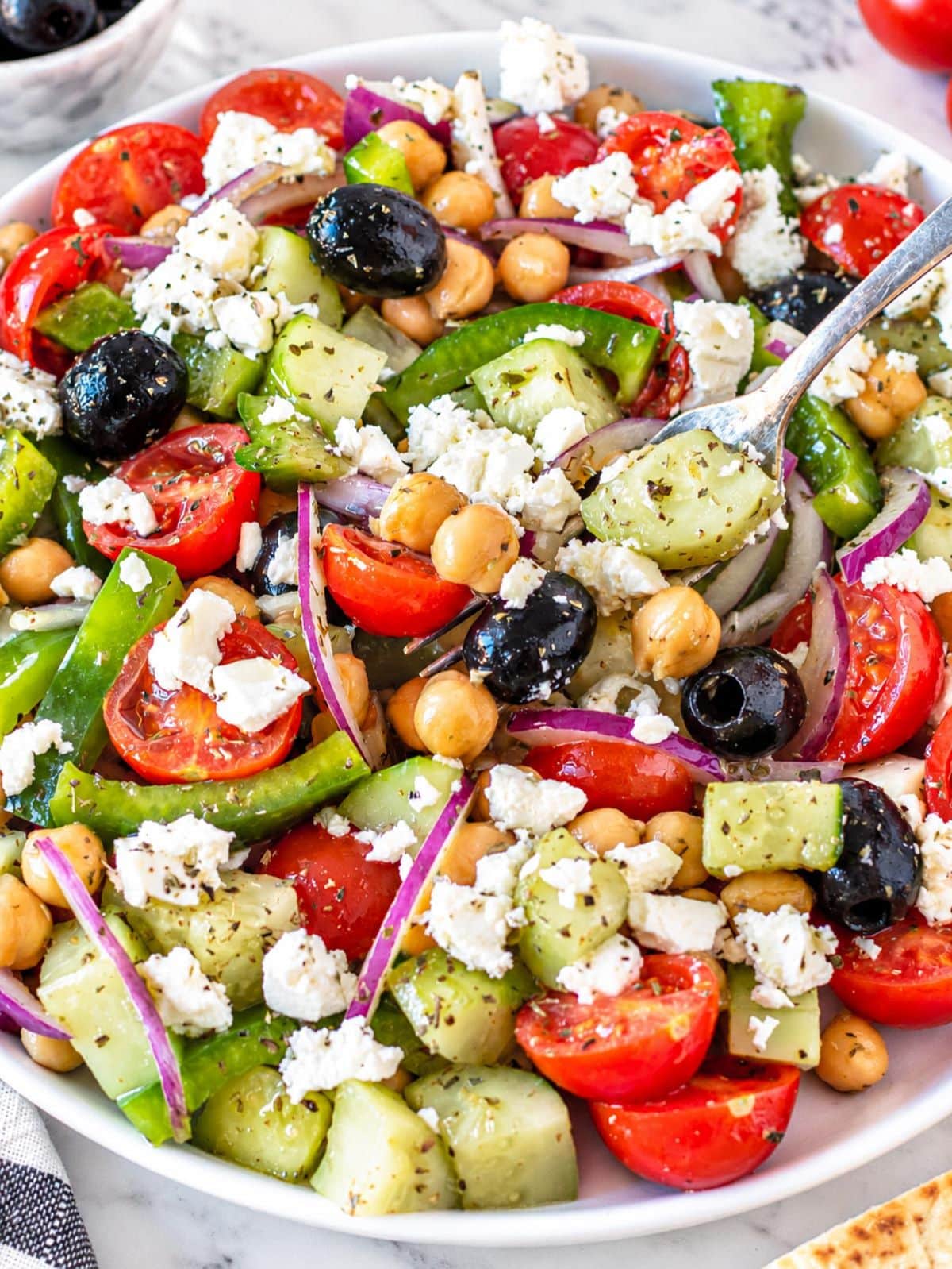 Greek chickpea salad with colorful vegetables, feta, olives, and glossy chickpeas.