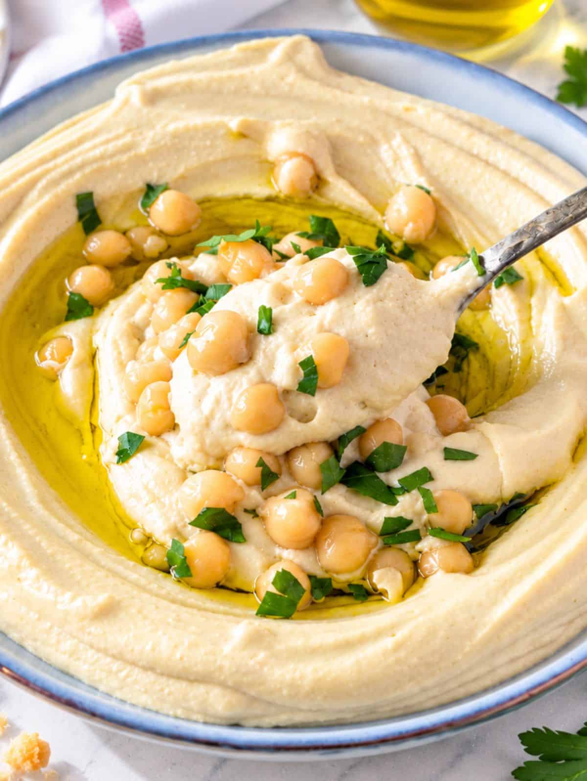 Macro close up of smooth hummus showing its silky texture, olive oil, chickpeas, and parsley.