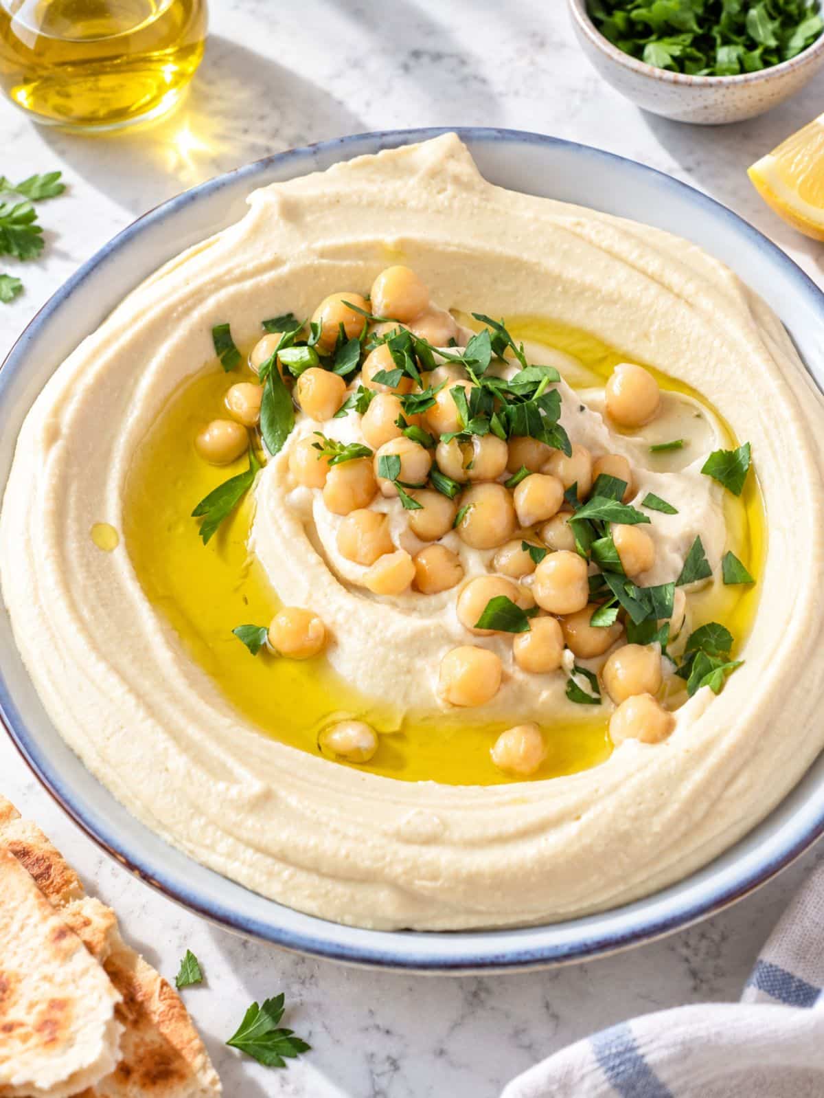 Smooth hummus showing its silky texture, olive oil, chickpeas, and parsley.