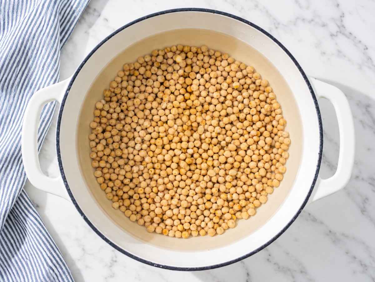 Step 1 Chickpeas simmering until very soft and tender in a pot on white marble.