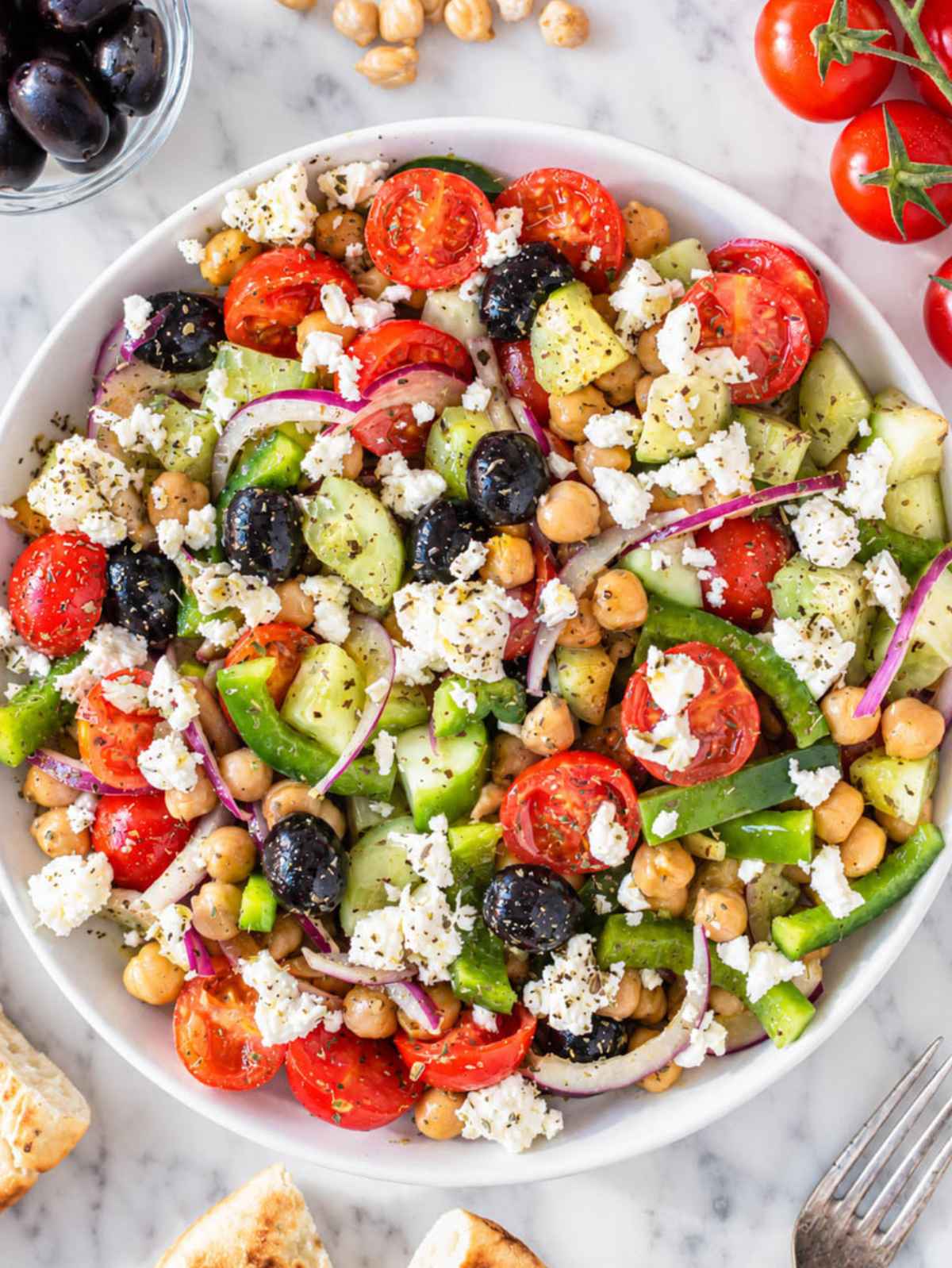 Top down of glossy chickpeas, feta, tomatoes, cucumber, olives, and pepper.