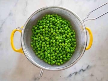 Blanched green peas in a sieve.