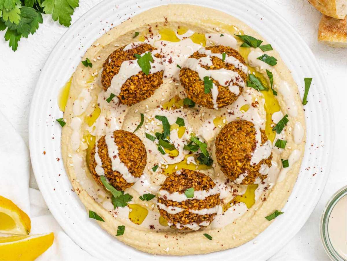 Falafel served on a bed or hummus, topped with tahini sauce, parsley, and sumac.