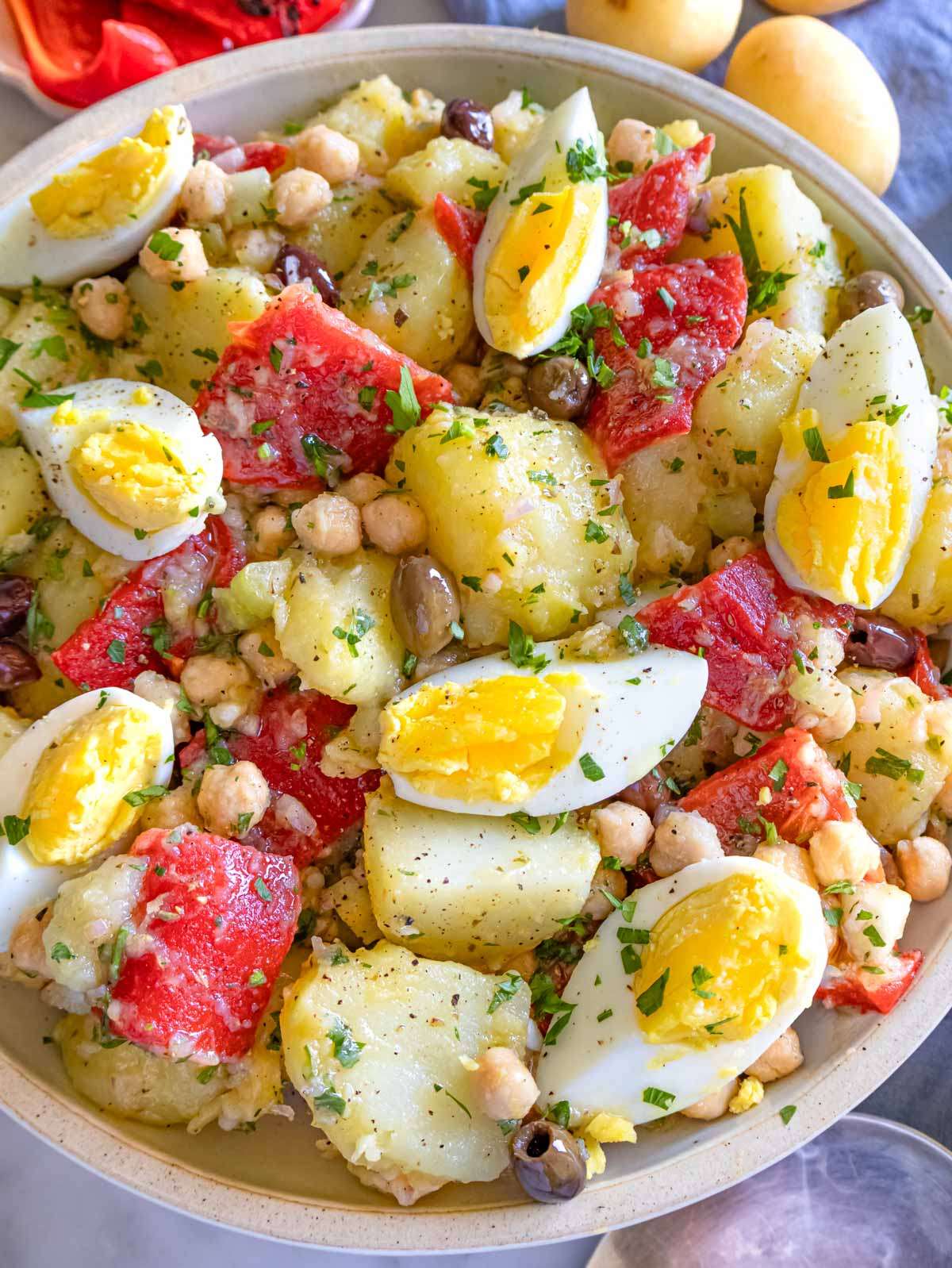 Close-up of Italian-style no-mayo potato salad with chickpeas, olives, and fresh herbs in a serving bowl.