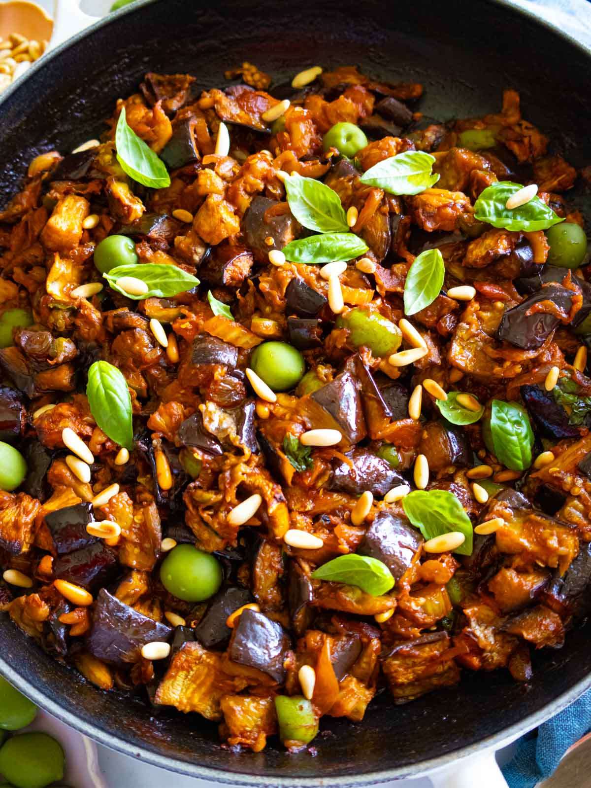 Close-up of authentic Sicilian caponata recipe with roasted eggplant, olives, pine nuts, and fresh basil in a rich sweet and sour sauce.