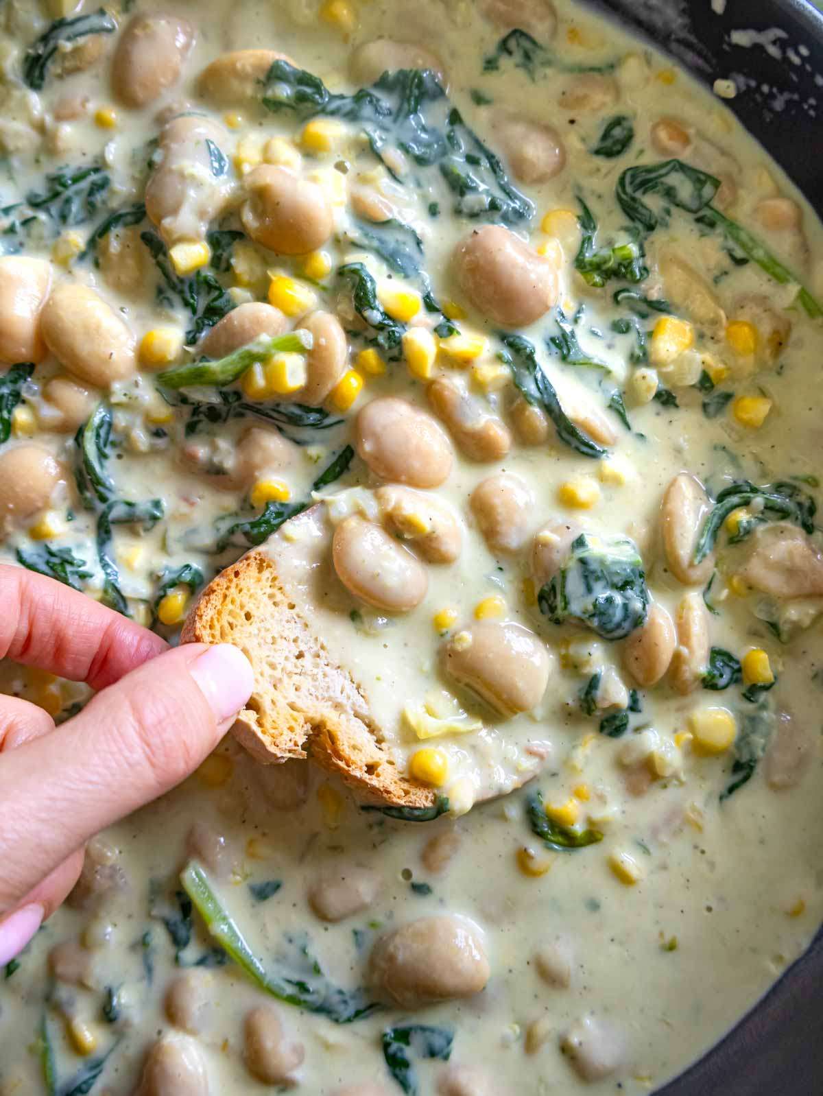 Close-up of creamy white beans, spinach, and corn in a rich Florentine-style sauce.