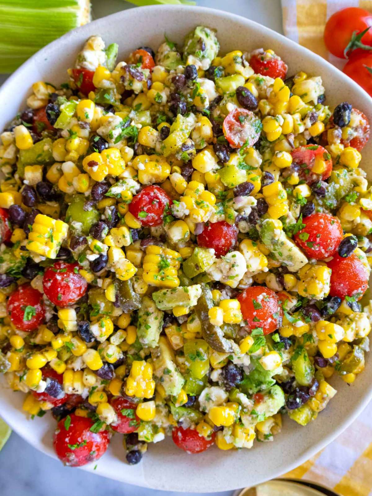 Close-up of fresh corn salad with black beans, avocado, cherry tomatoes, and cilantro lime dressing—served in a white bowl, showing vibrant summer colors and chunky texture.