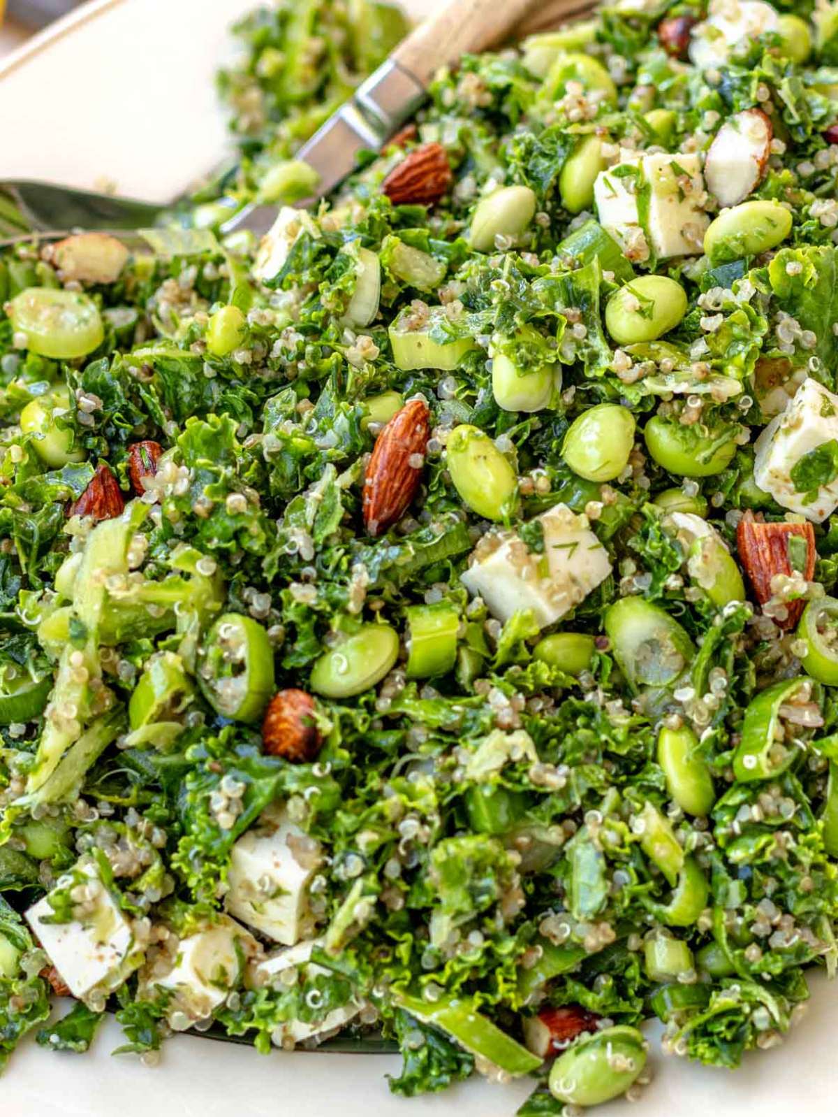 Close-up of kale quinoa salad in a white bowl, showing quinoa, kale, feta, edamame, almonds, and herbs tossed in lemon dressing