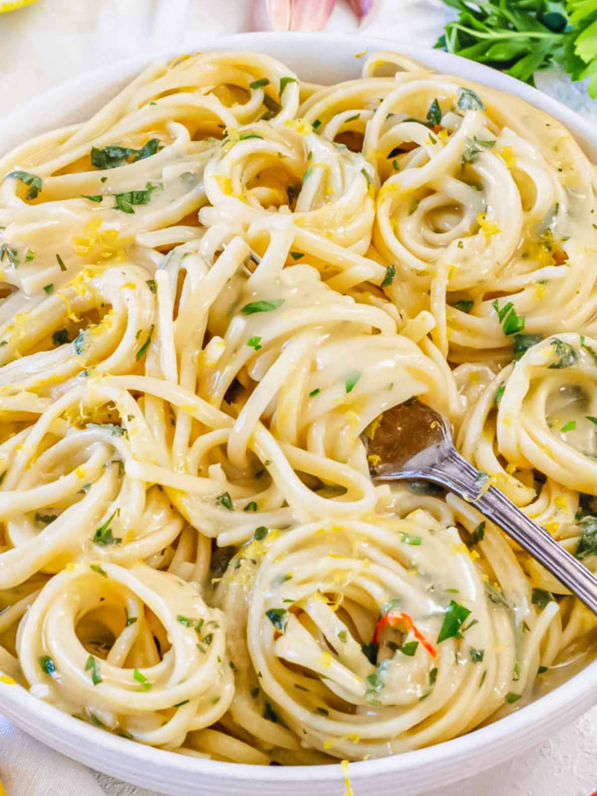 Close-up of lemon pasta without cream, twirled on a fork and garnished with fresh parsley and lemon zest.
