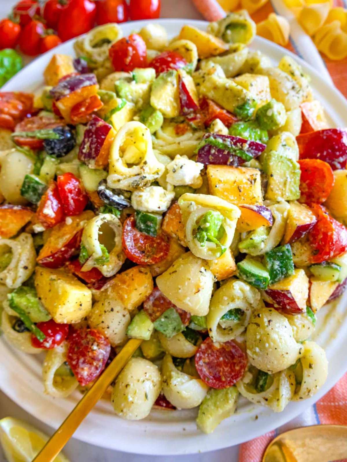 Close-up of summer pasta salad highlighting creamy avocado, juicy peaches, cherry tomatoes, and crumbled feta.