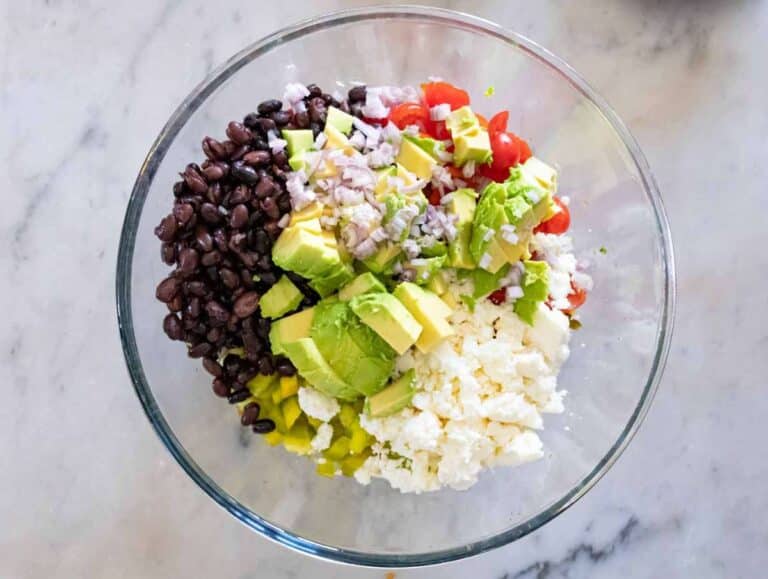 Corn, black beans, avocado, feta, onion, tomatoes, and bell pepper in the bowl with the dressing.