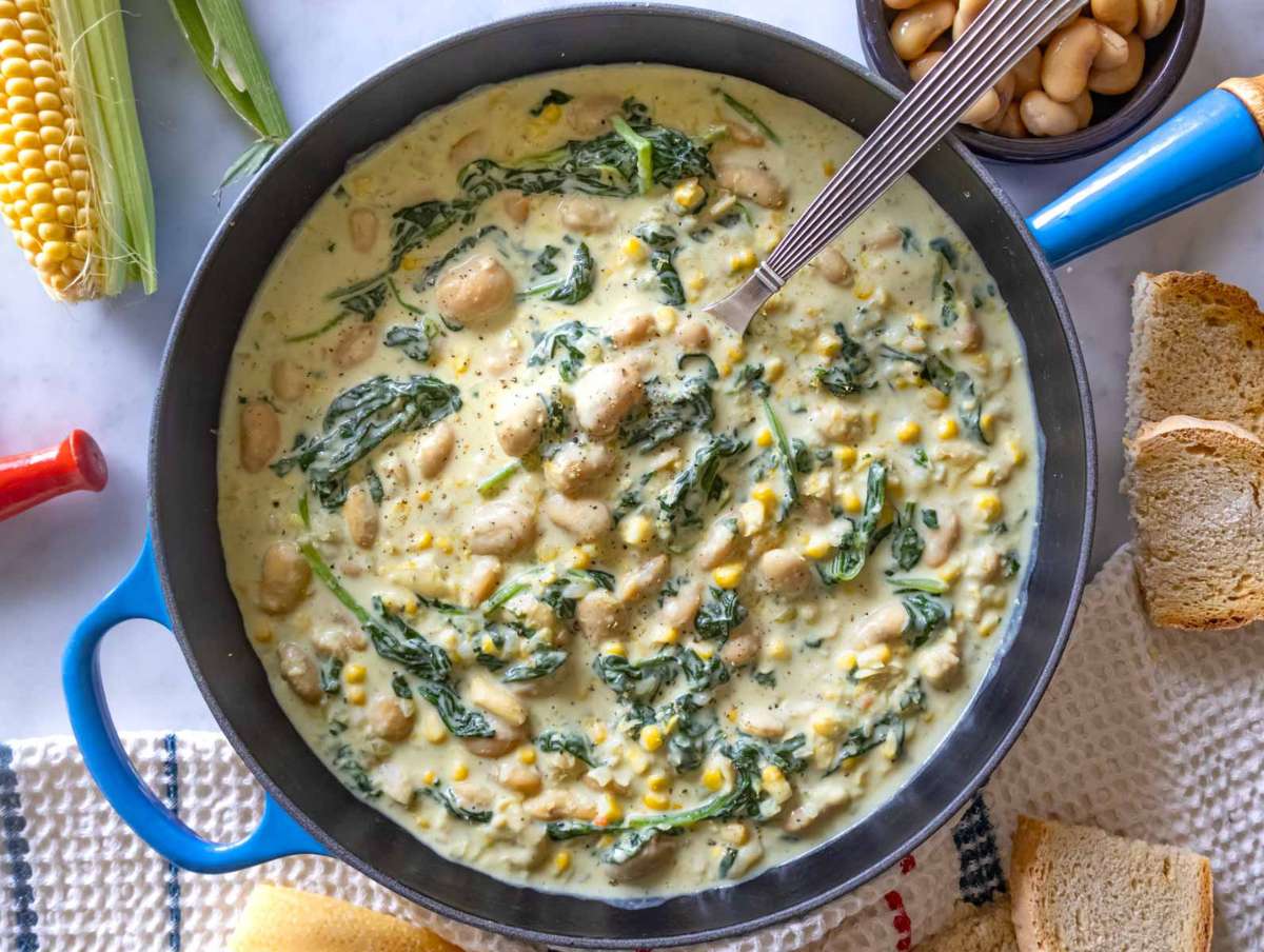 Creamy butter bean in Florentine sauce served in a blue skillet with bread.