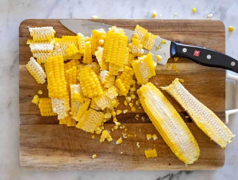 Cutting the kernels off the cob with a sharp knife on a cutting board.