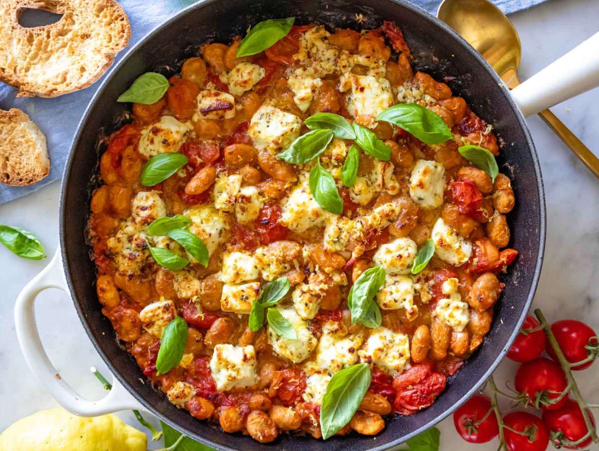 Feta-topped butter bean stew in a skillet, after broiling, topped with basil.