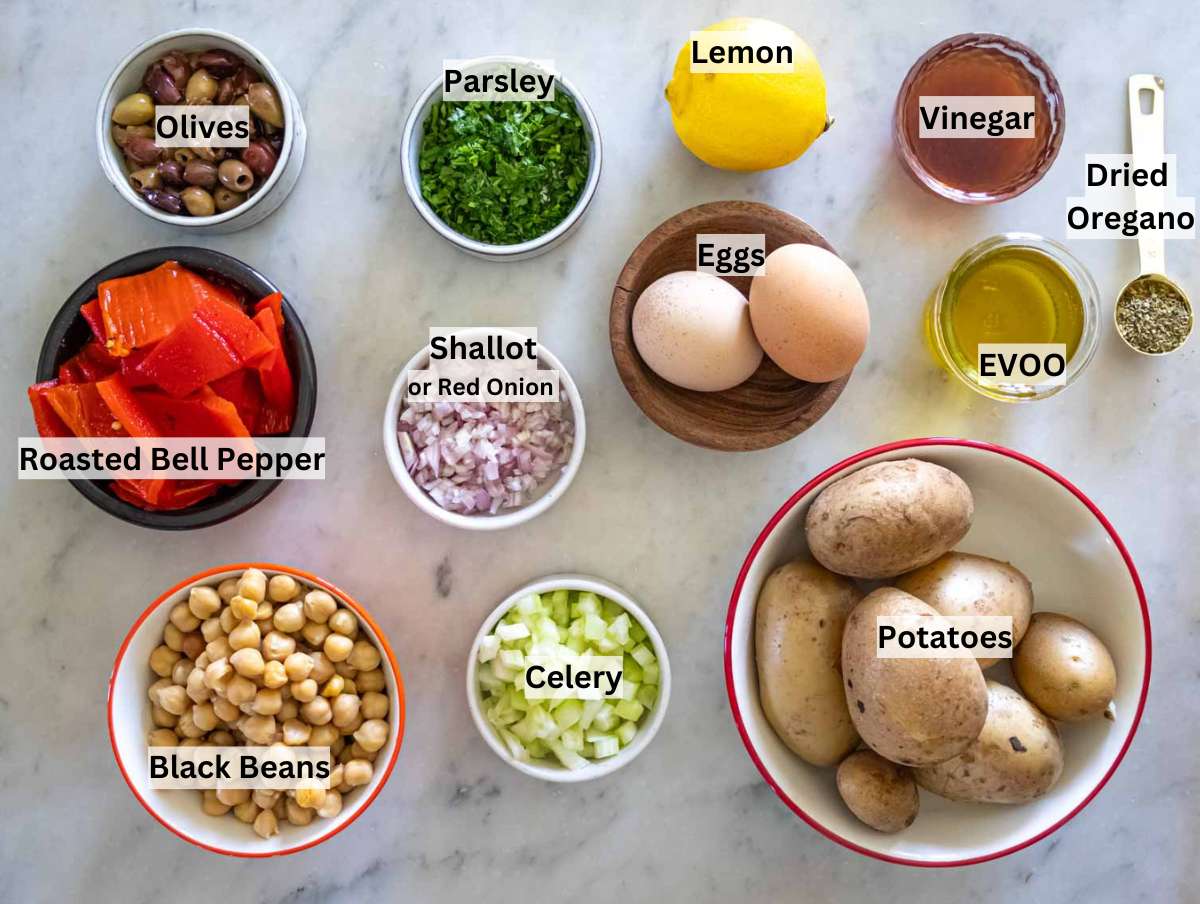 Flat lay of fresh ingredients for no-mayo potato salad, including potatoes, olive oil, red onion, chickpeas, and herbs.