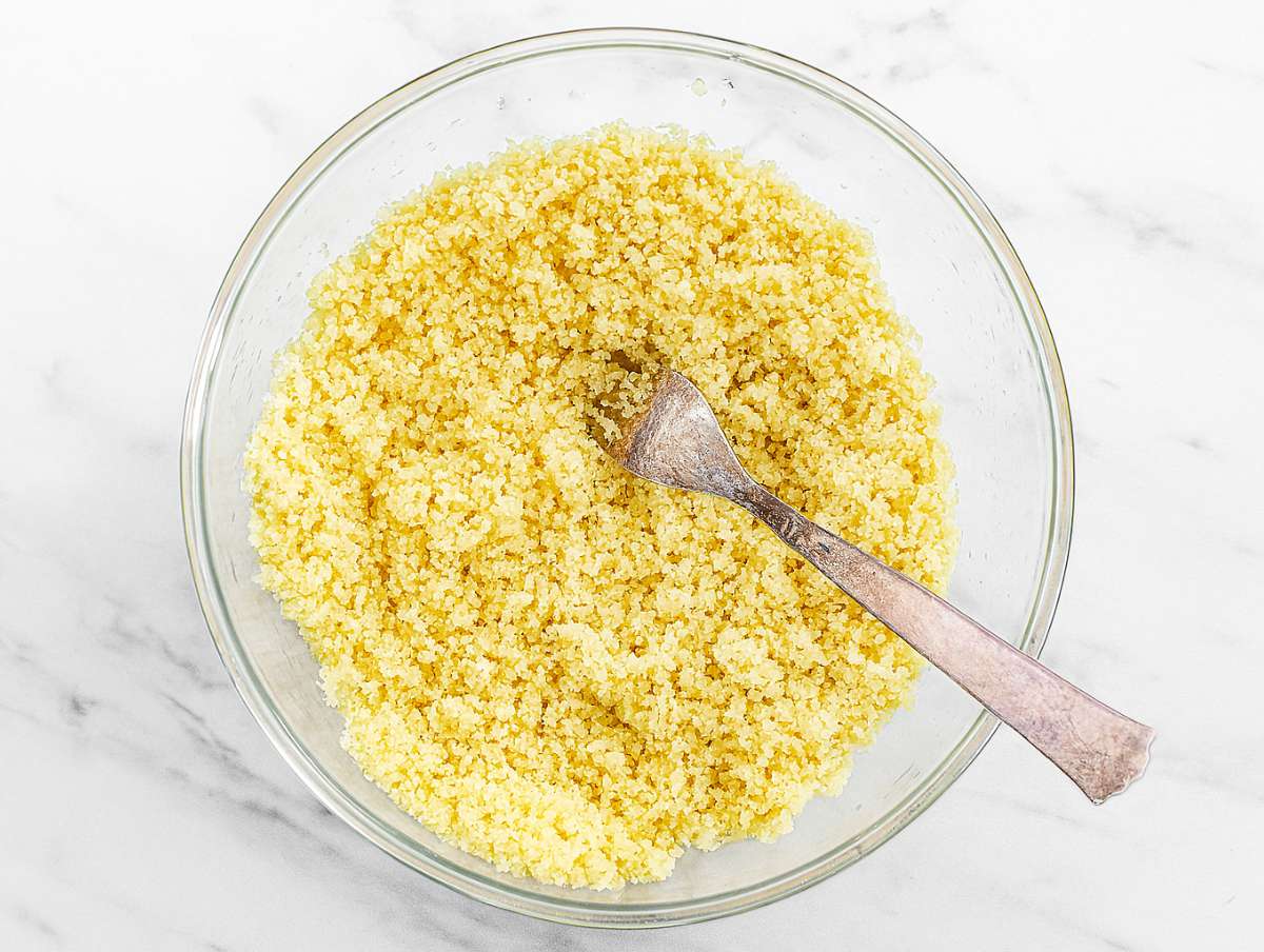 Fluffy couscous being fluffed with a fork after steaming.