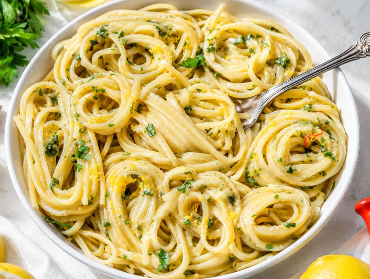 Fork in glossy Lemon Pasta served in white bowl in natural daylight.