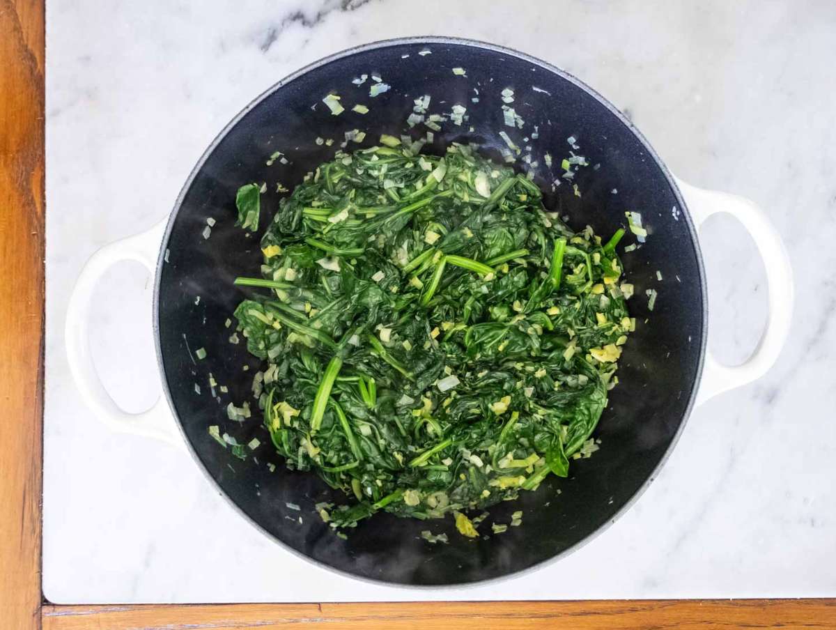 Fresh spinach wilting in pot with olive oil and salt for heart-healthy Greek one-pot meal.