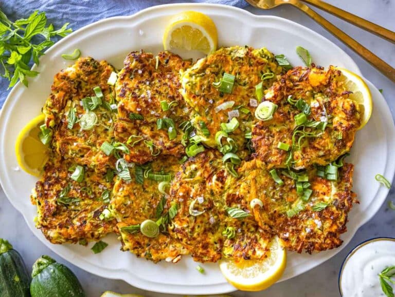 Freshly cooked zucchini patties served on a platter with fresh herbs and lemon wedges.